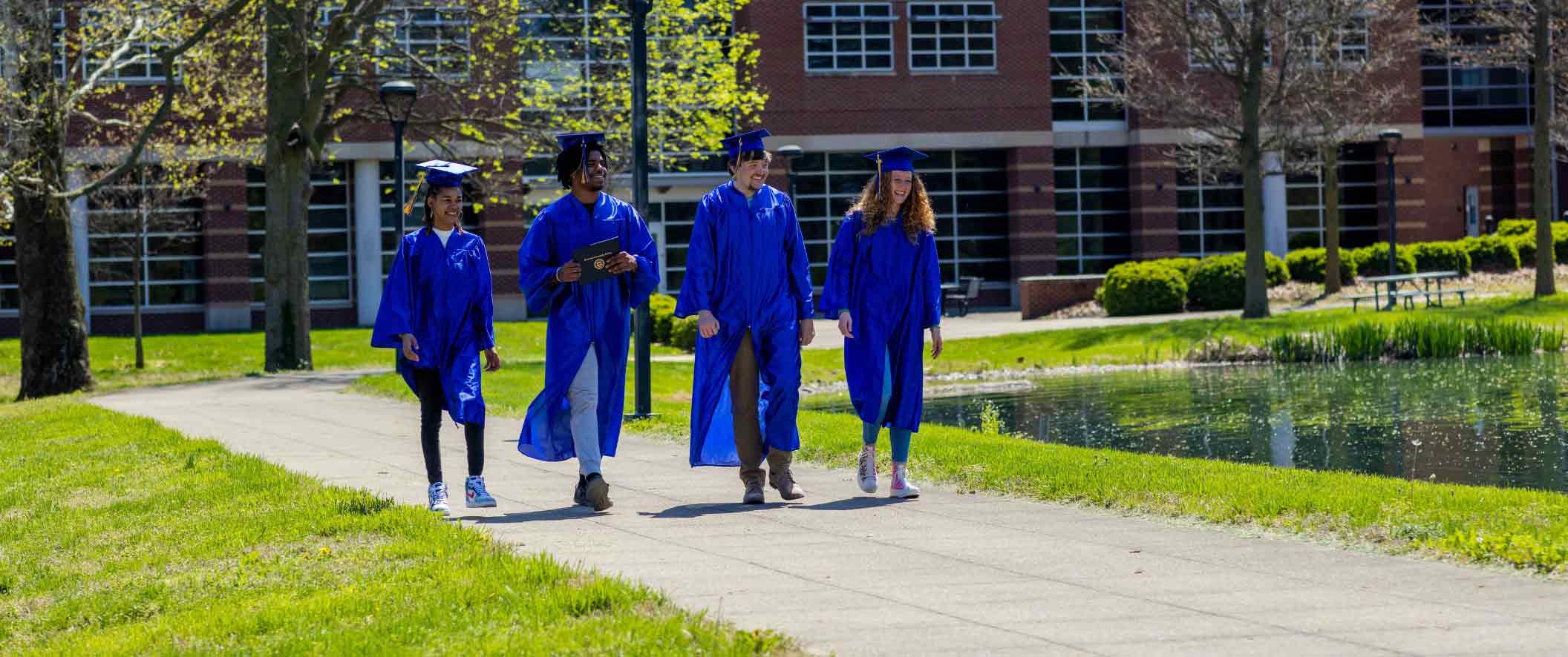 four students walking down the sidewalk in caps and gowns