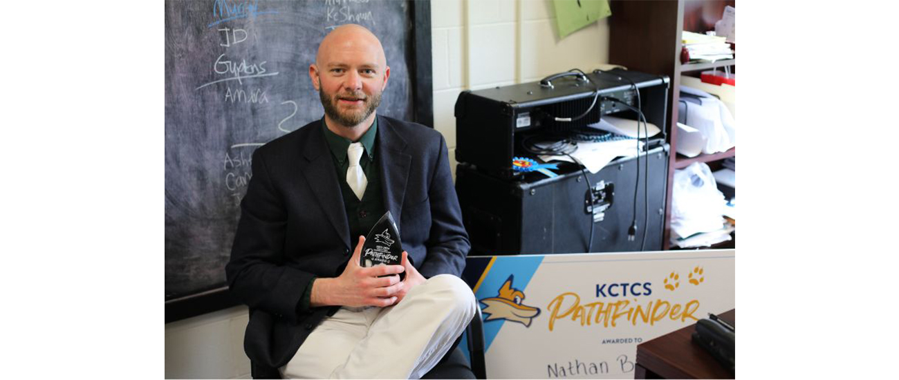 Nathan Britt sitting with his award in front of his chalkboard